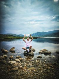 Man sitting on rock at lake against sky