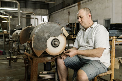 Craftsman using grinding machine while making creative wooden folding fan in shabby workshop