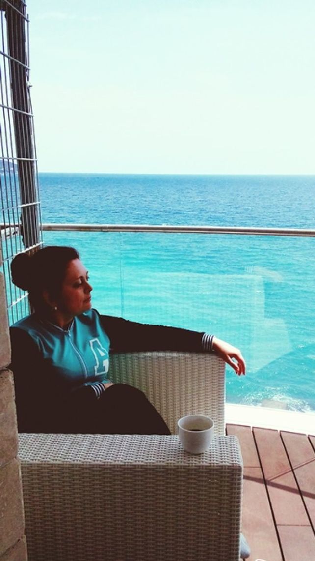 YOUNG WOMAN SITTING ON SEA AGAINST CLEAR SKY