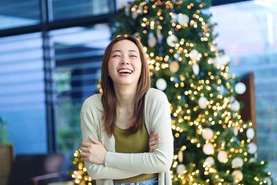 Portrait of young woman standing against christmas tree