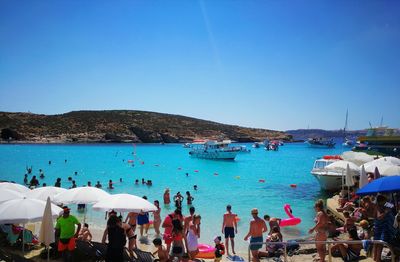 People on beach against clear blue sky