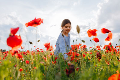 Young woman standing amidst yellow flowering plants on field against sky