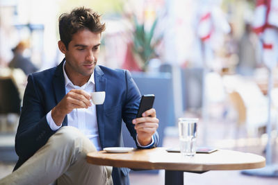 Businessman drinking coffee while using mobile phone