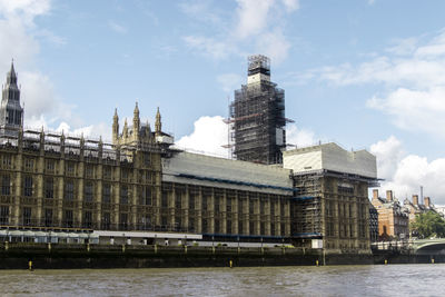 Buildings by river against cloudy sky