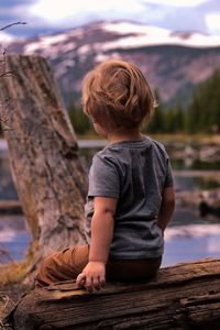 Rear view of boy sitting on log