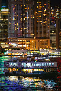 Illuminated modern buildings by river in city at night