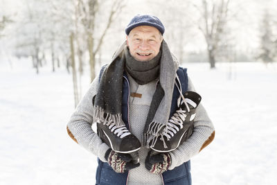 Smiling senior man with ice skates in winter forest