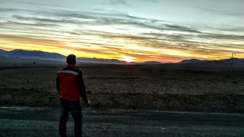 Rear view of man standing on landscape against sky during sunset