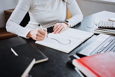 Female accountant writing question mark in a notepad on the background of laptop and calculator