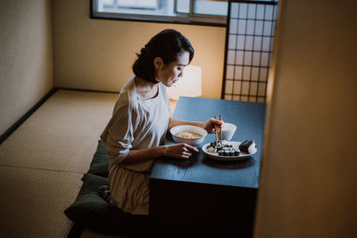 Side view of woman sitting on table at home