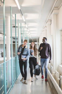 Male and female students talking while walking in corridor of university