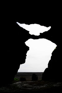 Silhouette rock formation in sea against sky