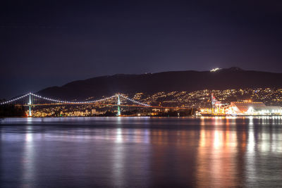 Illuminated bridge over river against sky at night