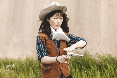 Young woman aiming gun while standing against wall