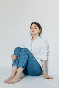 Young woman sitting on floor against white background