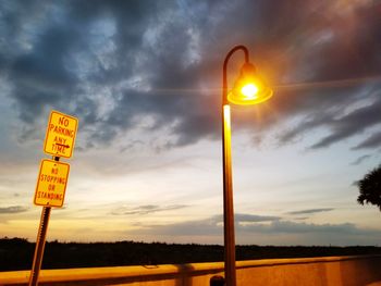 Road sign by street against sky during sunset