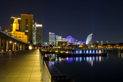 Illuminated buildings by river against sky at night