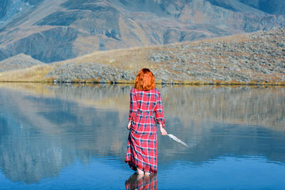 Rear view of woman holding feather while standing in lake by mountains
