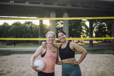 Portrait of smiling woman with arm around female friend holding volleyball