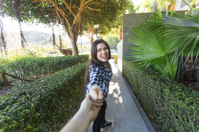 Portrait of smiling young woman standing on footpath amidst plants