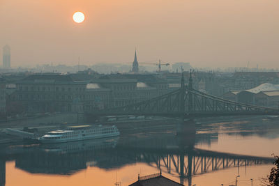 Bridge over river against buildings during sunset