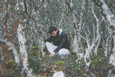 Young man sitting on tree trunk in forest