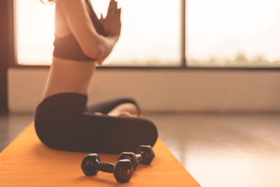 Low section of woman meditating while sitting on exercise mat at gym