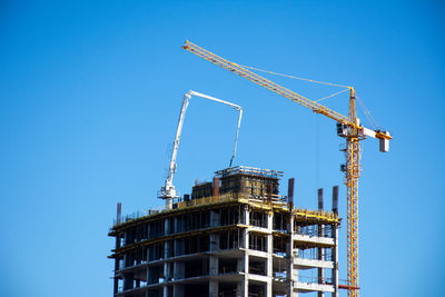 Low angle view of crane by building against clear blue sky