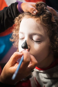 Cropped hand of woman applying black paint on boy nose