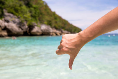 Close-up of hand showing thumbs down against sea