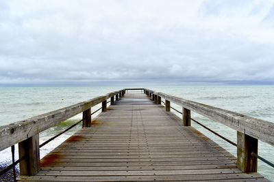 Empty wooden pier leading towards sea against sky