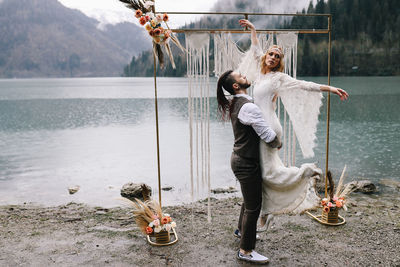 Two happy people in love the bride and groom in wedding outfits embrace by the lake and mountains