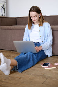 Young woman using digital tablet while sitting on sofa at home