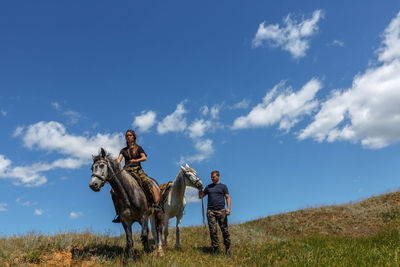 Woman riding horse with friend on field against sky