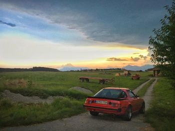 Car on road amidst field against sky during sunset