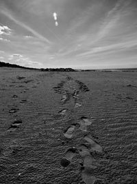 Footprints in sand at beach against sky