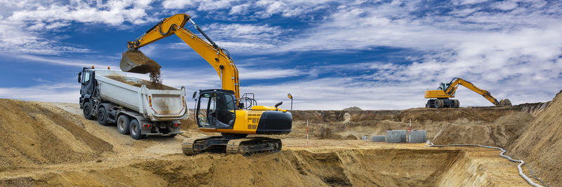 Excavator working on construction site with dramatic clouds on sky