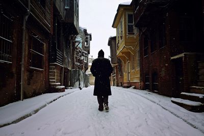 Rear view of man walking on snow covered street amidst buildings