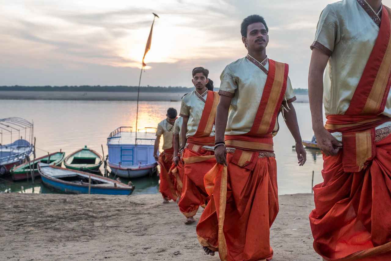 water, sky, real people, transportation, nautical vessel, standing, mode of transportation, sea, men, sunset, group of people, young adult, nature, adult, young men, beach, togetherness, emotion, outdoors