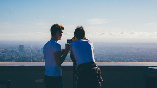 Rear view of couple standing against sea and cityscape