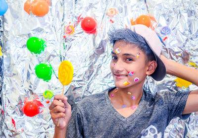 Portrait of boy holding lollipop by multi colored balloons