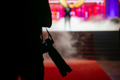 A cameraman with a black camera standing in front of the stage where a man is singing in concert.