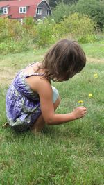 Side view of girl picking flowers while crouching on grassy field