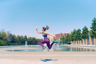 Full length of woman jumping against blue sky