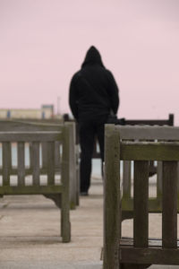 Rear view of man walking on pier against clear sky