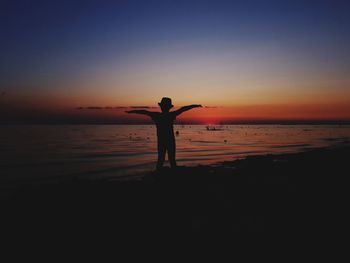 Silhouette man standing on beach against sky during sunset