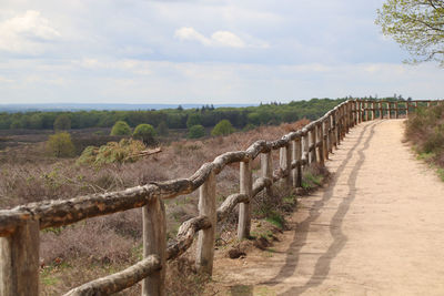 Wooden posts on footpath amidst field against sky