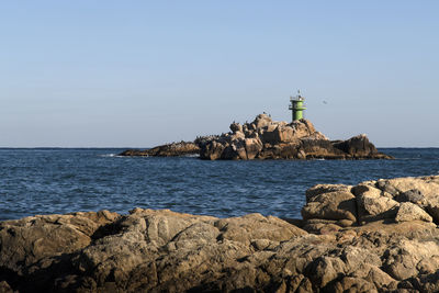 Lighthouse on rock by sea against sky