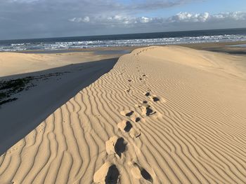 Footprints on sand at beach against sky