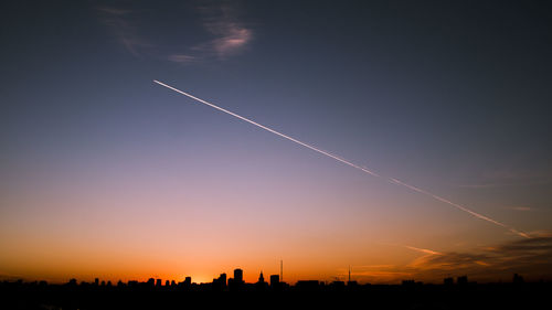 Silhouette vapor trail against sky during sunset